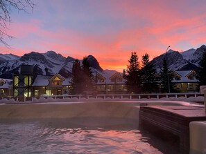 A resort with snow-covered mountains, a pool, and multiple chalet-style buildings.