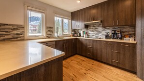 Eine moderne Küche mit dunklen Holzschränken, einer großen Kochinsel und Bergblick durch die Fenster.