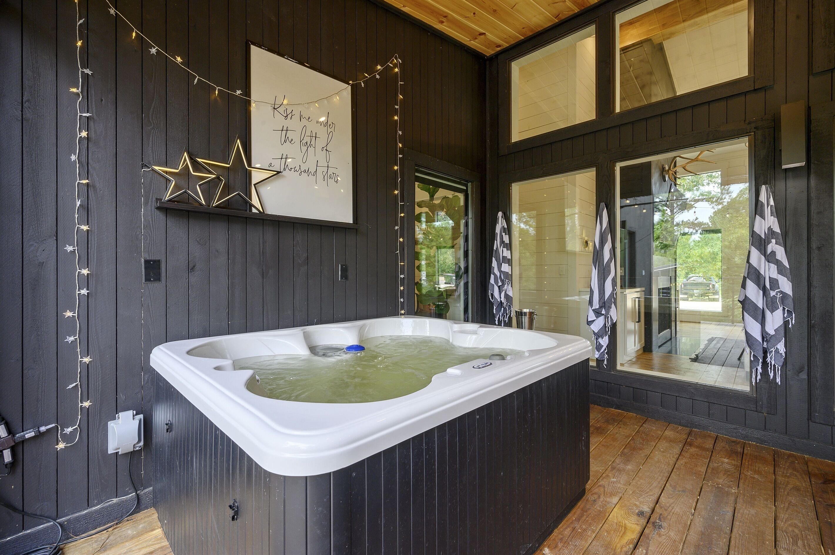 Ein moderner Wellnessraum mit einer großen Whirlwanne, Holzwänden und Blick ins Freie.