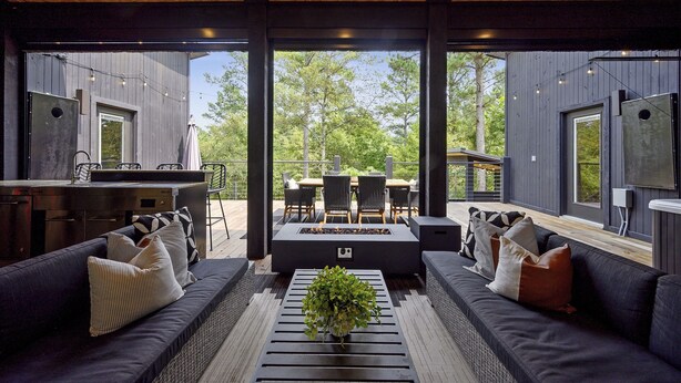 A modern outdoor living area with a sofa, a fire pit, and a dining set. - Woodland Cabin | Hot Tub · Fire Pit · Forest Views (Broken Bow)