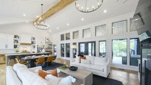 A spacious living area with a large white sofa, a coffee table, and a fireplace. There is a kitchen with white cabinets and a dining area with a table and chairs. - Woodland Cabin | Hot Tub · Fire Pit · Forest Views (Broken Bow)