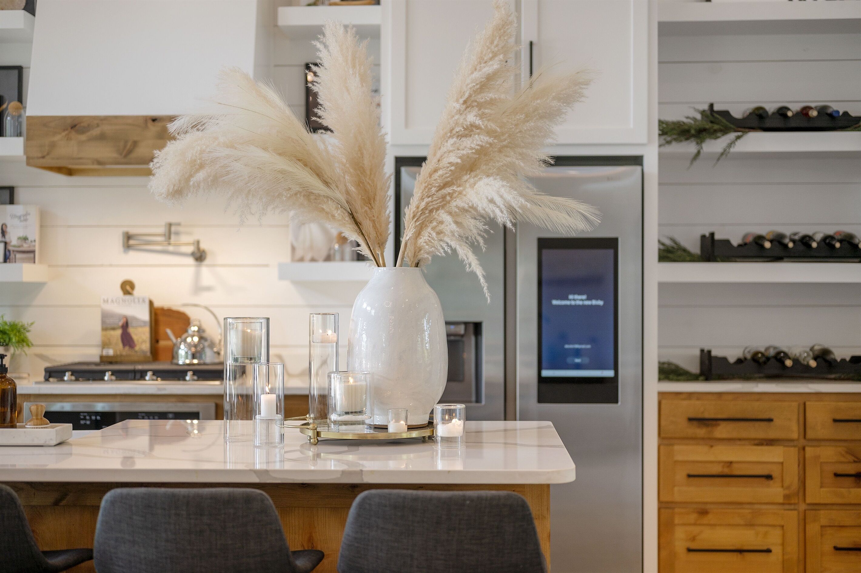Una cocina moderna con encimera de mármol blanco, un jarrón grande con plumas de pampa y una estantería para vinos en la pared.