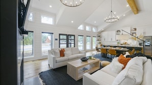 A spacious living room with a white sofa, coffee table, and a dining area with chairs and a table. - Woodland Cabin | Hot Tub · Fire Pit · Forest Views (Broken Bow)