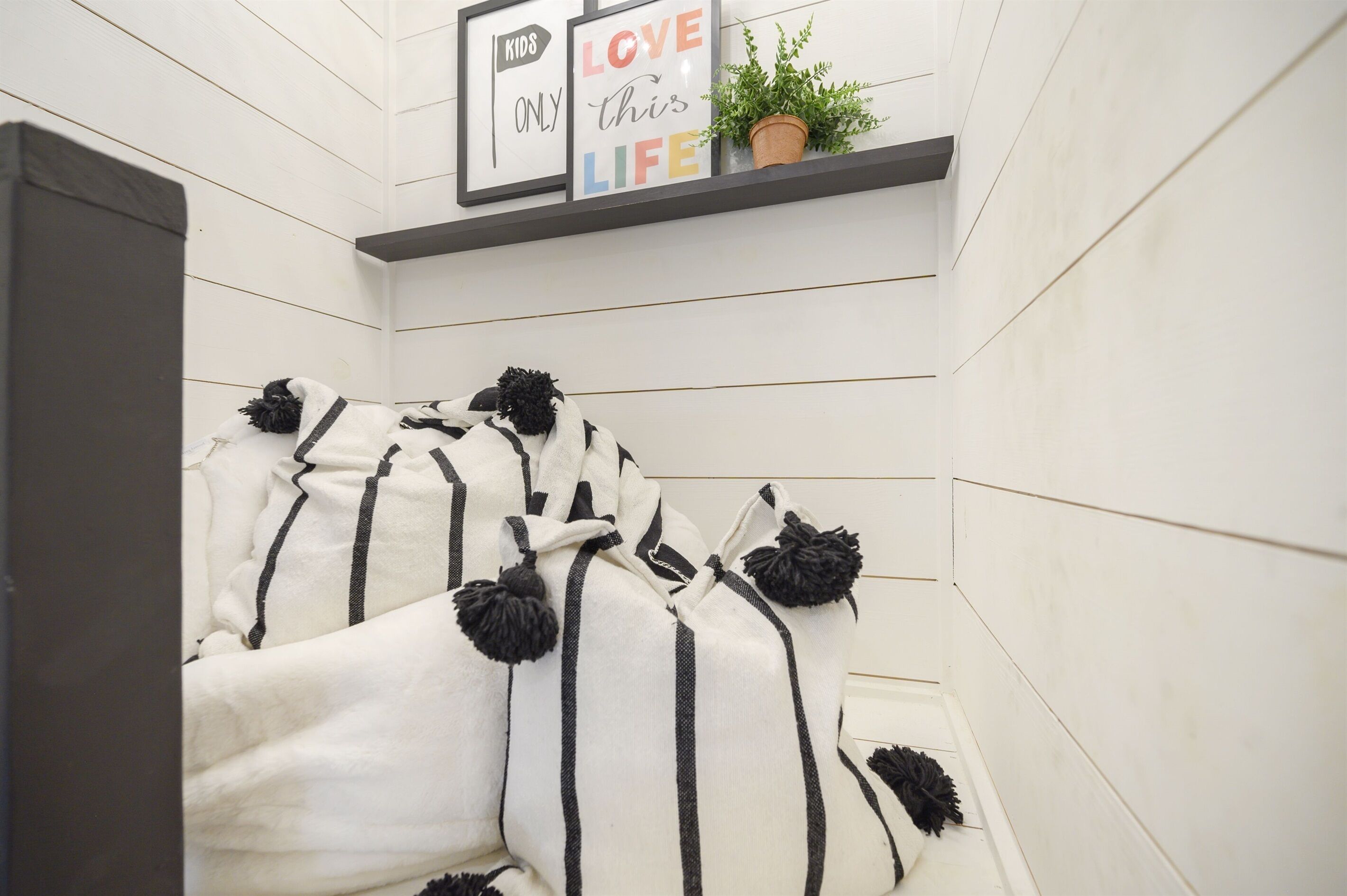 A bedroom with a bed covered in a striped blanket, a framed quote on the wall, and a potted plant.