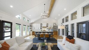 A spacious living area with a large white sofa, a coffee table with decorative items, and a dining area with a table set for four. - Woodland Cabin | Hot Tub · Fire Pit · Forest Views (Broken Bow)