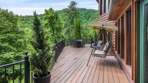 Une terrasse en bois avec des meubles d’extérieur, un pot de fleurs et une vue sur une colline boisée.