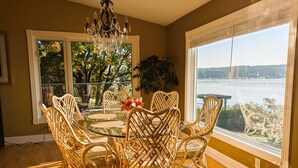 A dining area with a glass table surrounded by wicker chairs, a chandelier, and a view of a body of water through large windows. - Chateau Champlain Cottage (Penetanguishene)