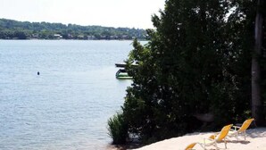 A beach with a row of yellow lounge chairs facing the water, a small dock, and a forested area in the background. - Chateau Champlain Cottage (Penetanguishene)