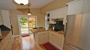 A kitchen with wooden flooring, white cabinets, a stainless steel refrigerator, and a view through the glass door. - Chateau Champlain Cottage (Penetanguishene)