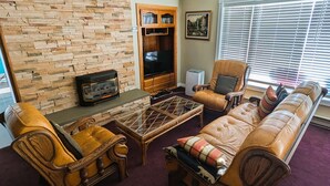 A living room with a stone wall, a fireplace, a television, a bookshelf, and a window with blinds. - Chateau Champlain Cottage (Penetanguishene)
