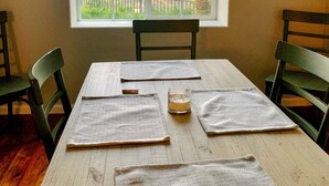 Een eettafel met placemats, een kaars en stoelen in een kamer met een groot rondboogvenster met uitzicht op een landschap.