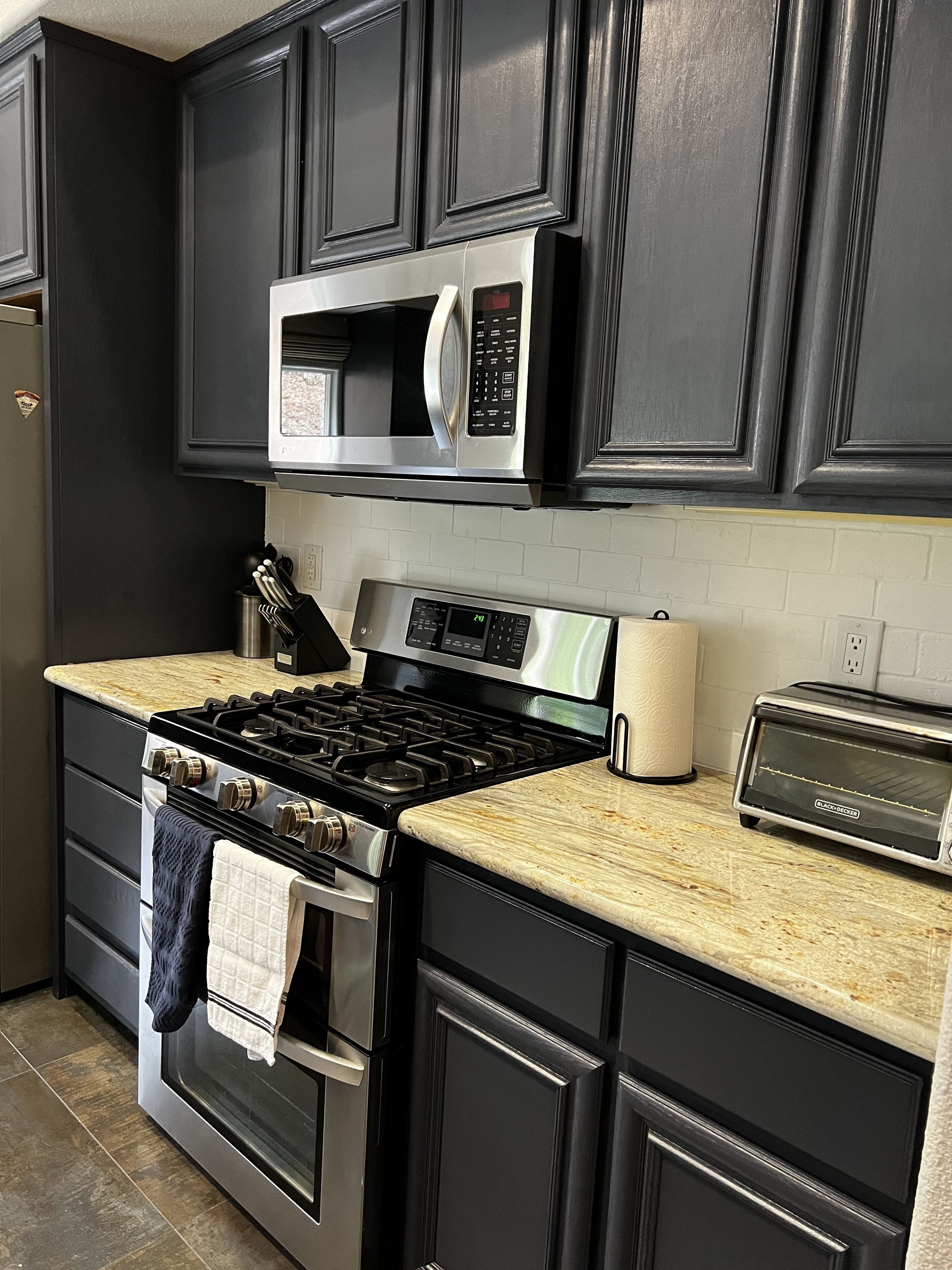 A kitchen with dark cabinetry, a stainless steel stove, a microwave, and a toaster.