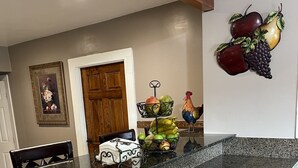A kitchen with a granite countertop, wooden stools, a fruit basket, and a rooster decoration. - Casa Cardoza (Los Angeles)