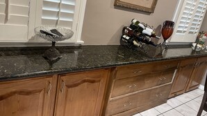 A kitchen with a granite countertop, wooden cabinets, a wine rack, and a framed picture on the wall. - Casa Cardoza (Los Angeles)