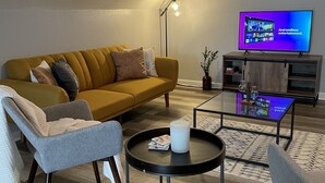 Una sala de estar moderna con un sofá, dos sillones, una mesa de centro y un televisor de pantalla plana.