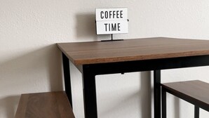 Una pequeña mesa de madera con un letrero que dice 'COFFEE TIME' sobre una pared lisa.