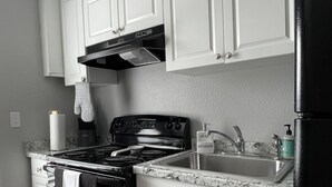 Una cocina con gabinetes blancos, una estufa negra y un lavaplatos de acero inoxidable.