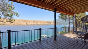 A wooden deck with a railing overlooking a body of water, a table, and chairs.