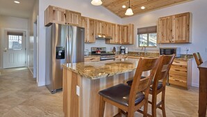 A modern kitchen with wooden cabinets, a stainless steel refrigerator, and a granite countertop island with bar stools.