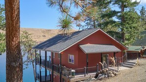 A red cabin with a balcony overlooking a lake, surrounded by trees.