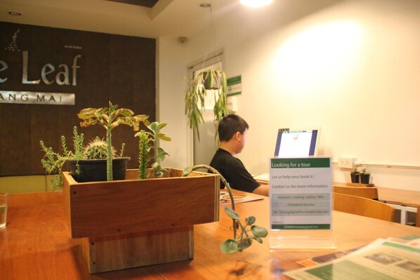 A reception desk with a signboard for tours, wooden furniture, and potted plants. - The Leaf Service Apartment (Chiang Mai)