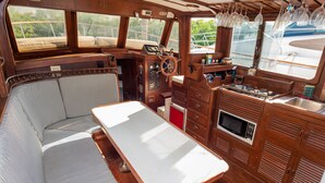 Cabina de barco con interior de madera, timón, mesa y banca.