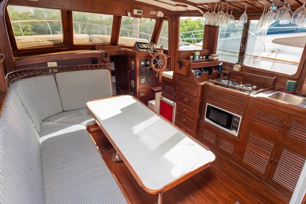 A boat cabin with a wooden interior, a steering wheel, a table, and a bench.