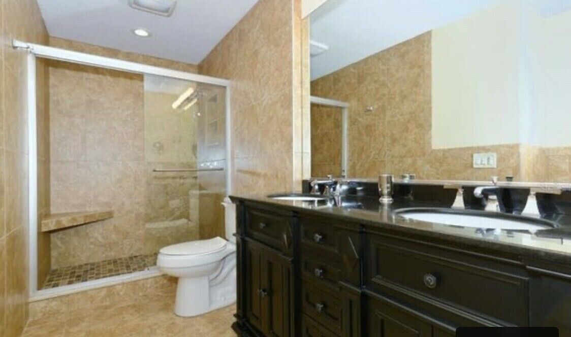 A bathroom with a shower, toilet, and dark wooden vanity with a sink.