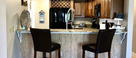 A kitchen with a central island, two bar stools, wooden cabinets, and a stainless steel refrigerator.