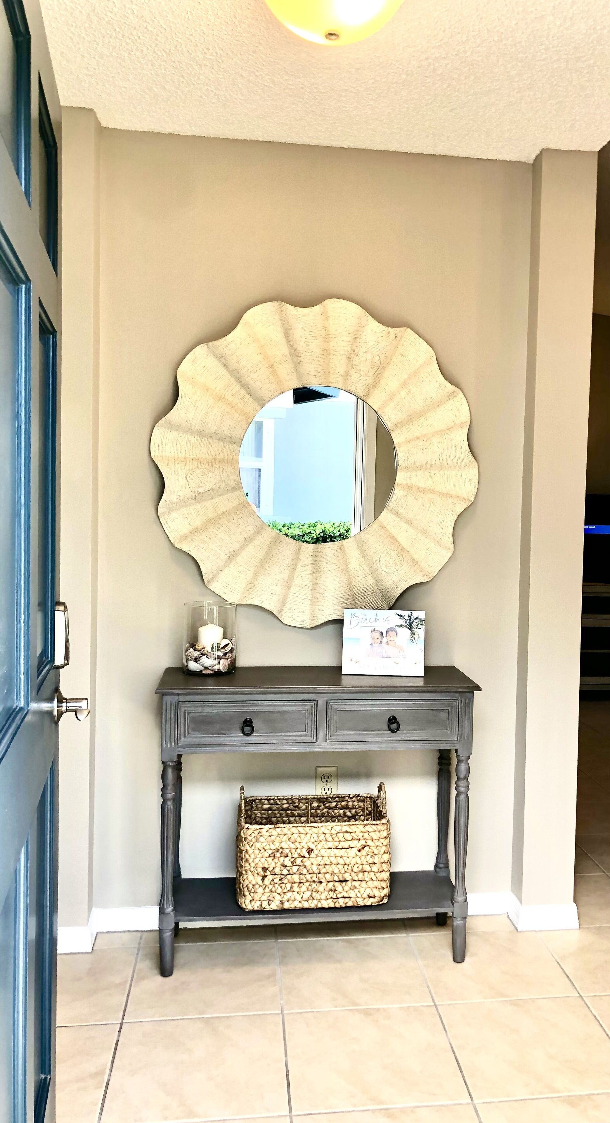 Une console en bois foncé, ornée d’un miroir décoratif, d’une photo encadrée et d’un panier tressé.