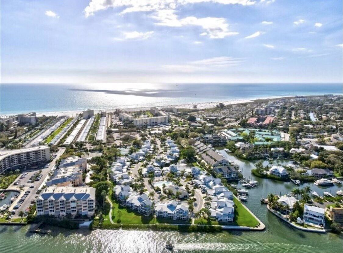 An aerial view of a coastal residential area with multiple buildings, a marina, and a beach.