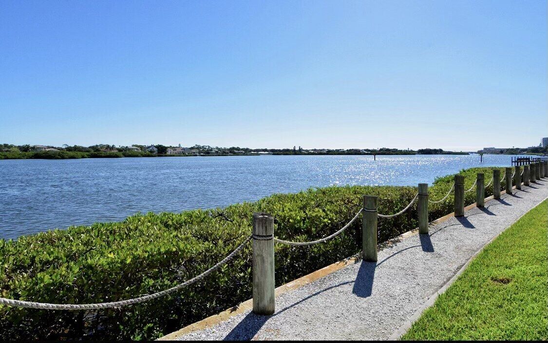 Un passeig marítim amb un camí herbaci, una tanca metàl·lica i una vista despejada de l'aigua.