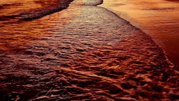 Une plage avec une longue étendue de sable humide qui descend vers la mer, sous un ciel au coucher du soleil.