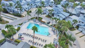 Un quartier résidentiel doté d’une piscine, entourée de palmiers et de maisons.