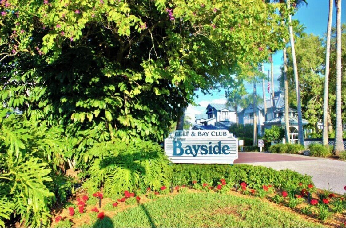 Schild für Bayside Golf & Bay Club mit gepflegtem Garten und Palmen im Hintergrund.