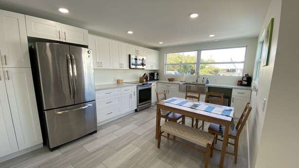 Una cocina moderna con armarios blancos, electrodomésticos de acero inoxidable y una mesa de comedor de madera con sillas.