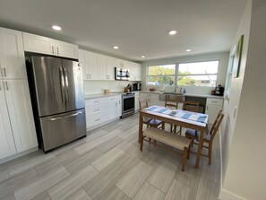 A modern kitchen with white cabinets, stainless steel appliances, and a wooden dining table with chairs. - Beautiful Remodeled Home on the Water! 40 ft dock & short walk to private beach! (Key Largo)