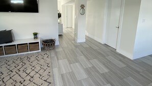 Un amplio salón con televisión de pantalla plana, un banco y una alfombra estampada.