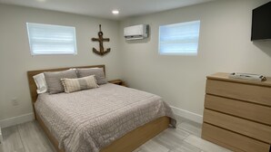 Un dormitorio con cama, cómoda y dos ventanas.