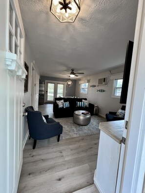 A spacious living area with a dark blue armchair, a black sofa with patterned cushions, a round coffee table, and a ceiling fan. - JOMO - Unit 2 TriTerrace *Relax Lakefront *Enjoy Fam (Rocky Mount)