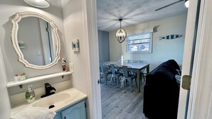 A bathroom with a large mirror, a sink, and toiletries. There is a dining area with a table and chairs, and a ceiling fan. - JOMO - Unit 2 TriTerrace *Relax Lakefront *Enjoy Fam (Rocky Mount)