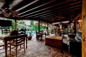 Un espacio de estar al aire libre cubierto con mobiliario de madera, piscina y plantas en macetas.