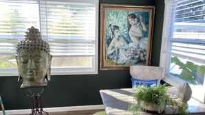 A room with a Buddha statue, a painting, and a bench with plants.