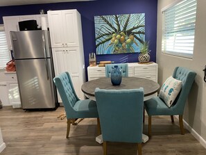 A modern kitchen with a stainless steel refrigerator, white cabinets, and a dining area with teal chairs and a round table. - ARLINGTON PARK COTTAGE 🌴SELBY GARDENS 🌺 MARINA JACKS 🛥 O’LEARYS 🌅 A 1 MILE WALK😎 (Sarasota)