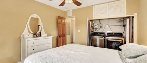 A bedroom with a bed, a ceiling fan, a dresser with a mirror, and a built-in washer and dryer.