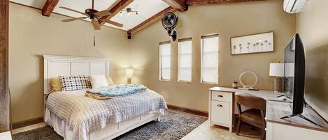 A bedroom with a bed, a desk, a chair, a ceiling fan, and a wall-mounted air conditioner.