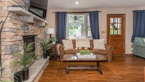 A living room with a stone fireplace, a brown leather sofa, a wooden coffee table, and a blue door.