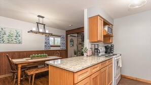 A kitchen with wooden cabinetry, a granite countertop, and a dining area with a wooden table and bench.