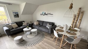 Un saló modern amb un sofà gris, dues taules rodones blanques i una taula de menjador amb cadires.