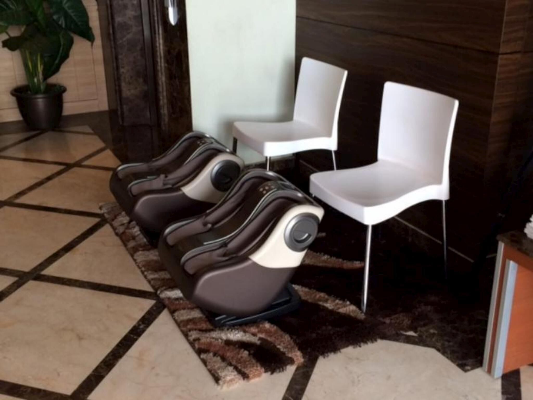 Zona de sillones de masaje con tres sillones masajeadores y dos sillas blancas, una planta en maceta y suelo de baldosas.